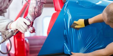 Professional worker spraying red paint on a car body