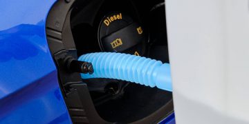 Close up filling of diesel exhaust fluid from canister into the tank of blue car for reduction of air pollution. Environmental or eco friendly solution.