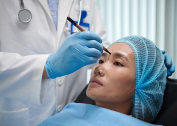 Plastic surgeon marking areas on face of young Asian woman before doing procedure
