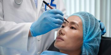 Plastic surgeon marking areas on face of young Asian woman before doing procedure