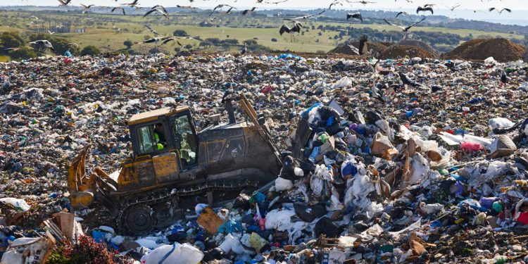 Heavy machinery shredding garbage in an open air landfill. Waste